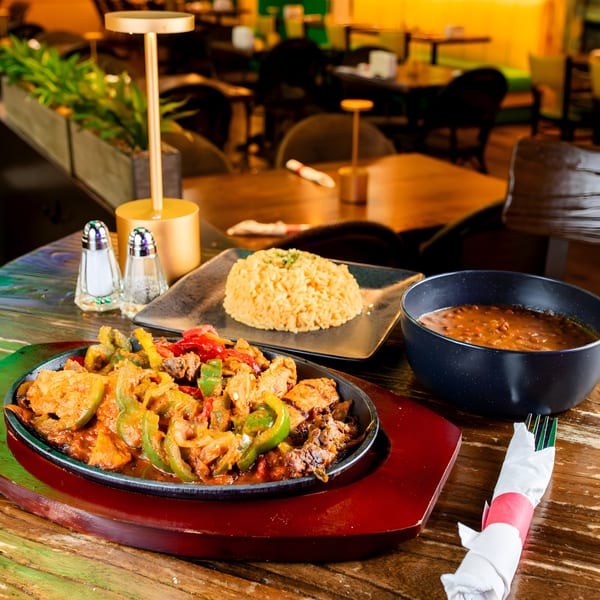 Sizzling fajitas with chicken, peppers, and onions, served with rice and beans on a wooden table.