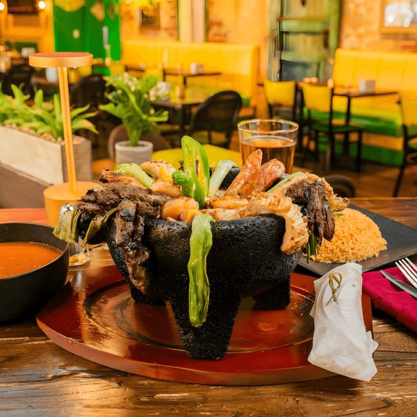 Molcajete with grilled meats, shrimp, and peppers, served with rice, salsa, and a beer.