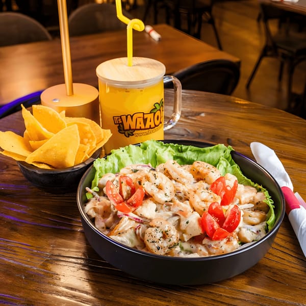 Shrimp ceviche with lettuce and tomatoes, tortilla chips, and a yellow drink on a wooden table.