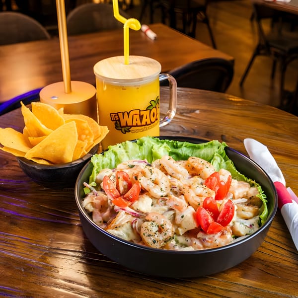 Shrimp ceviche with lettuce, tomatoes, and red onions, served with tortilla chips and a drink.