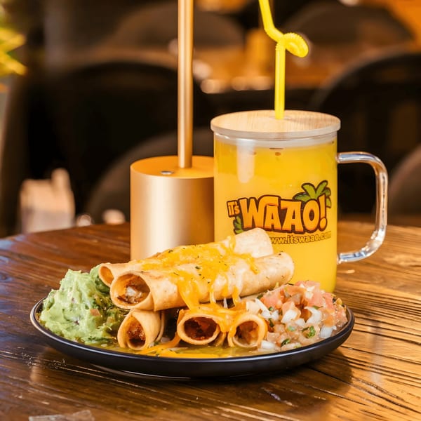 A plate of cheesy taquitos with guacamole and pico de gallo, next to a yellow drink.