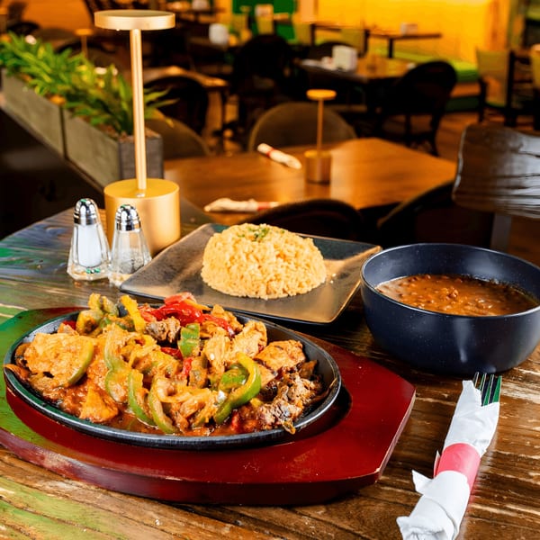Sizzling fajitas with rice and beans on a rustic wooden table in a restaurant setting.