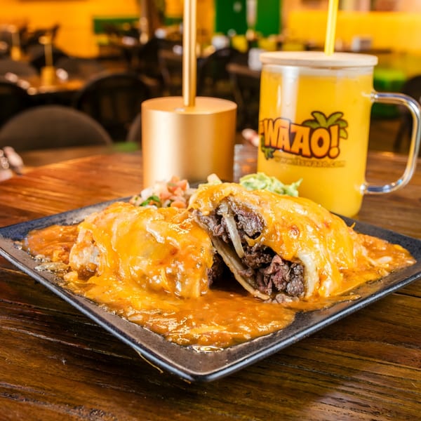 A beef burrito smothered in cheese sauce, with a side of salsa and a yellow drink.