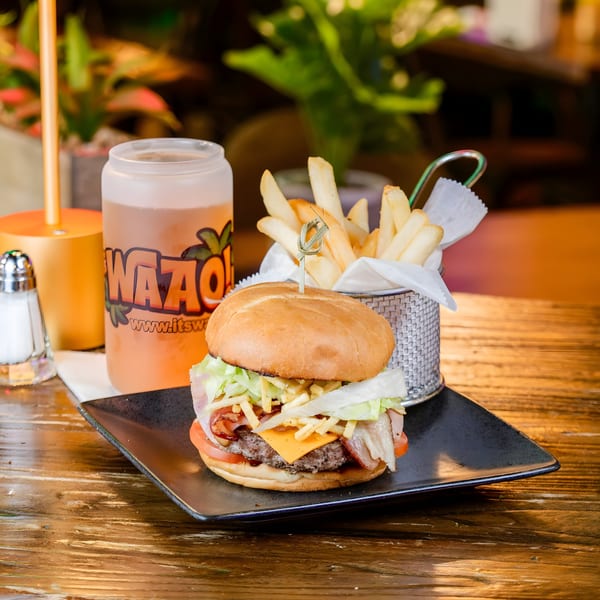 Cheeseburger with bacon, lettuce, tomato, and fries, alongside a drink on a wooden table.